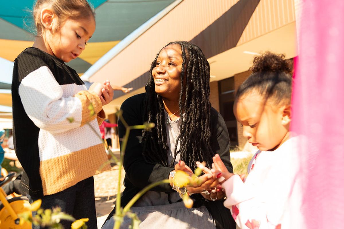 teacher kneeling down smiling with children outside