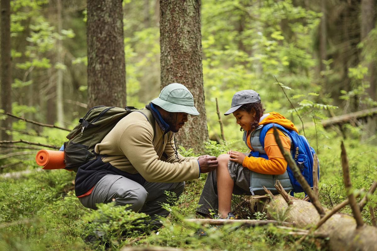 father putting bandaid on daughters knee in forest